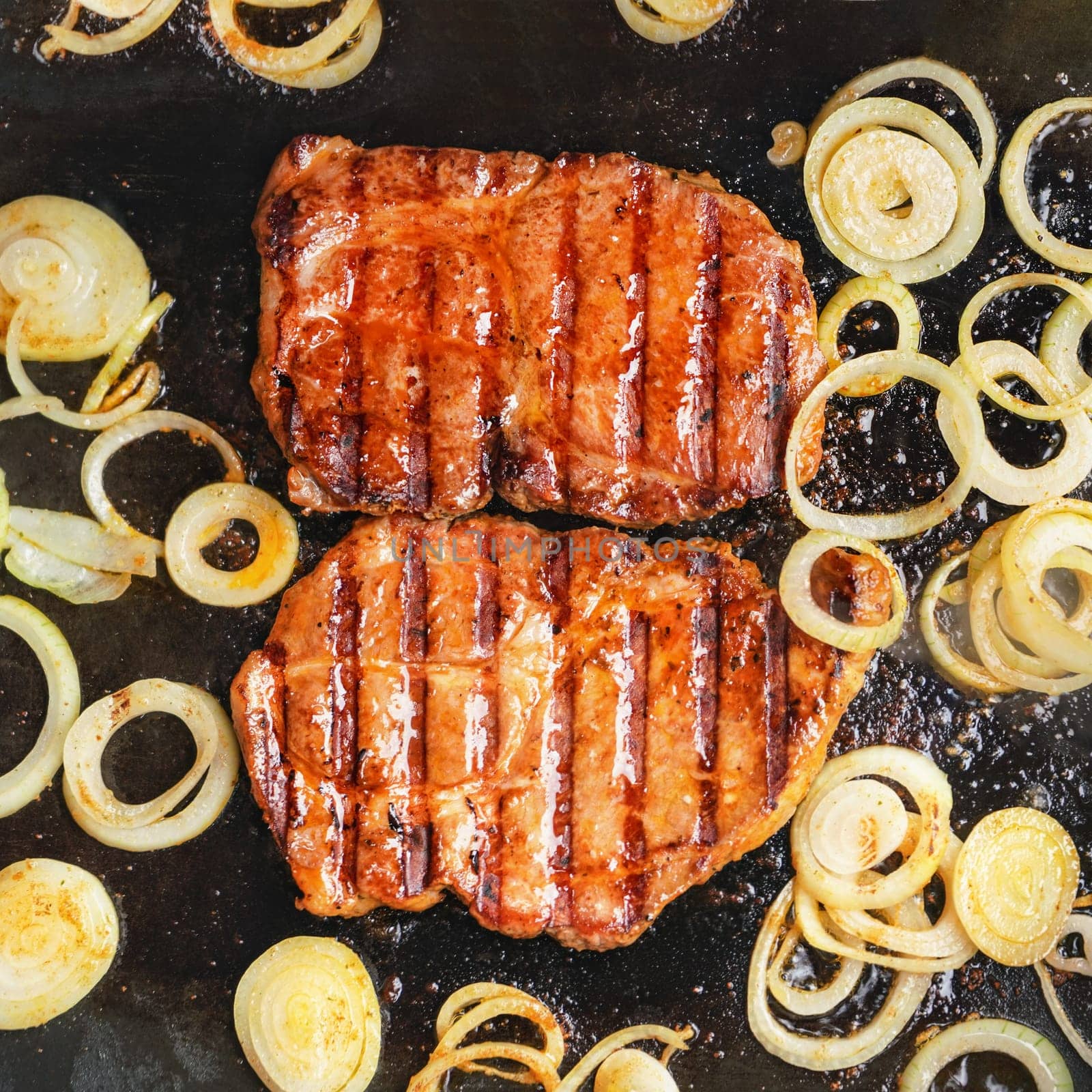 Two pork cutlets steaks and onion cut to slices, grilled on electric grill, overhead view by Ivanko
