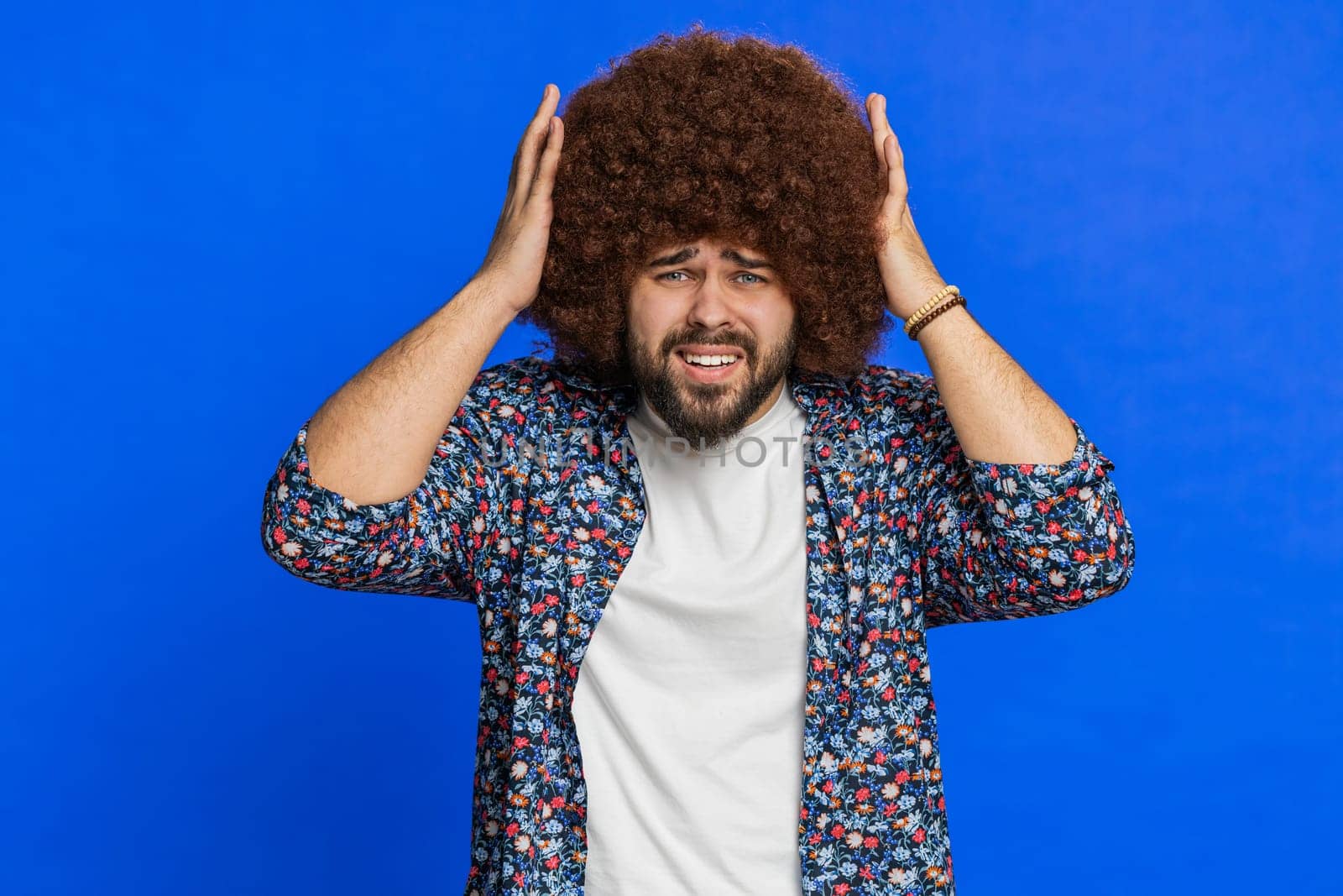 Sad young man with Afro hairstyle wig feeling hopelessness loneliness, nervous breakdown, loses becoming surprised by lottery results, bad fortune, loss unlucky news. Stylish guy on blue background