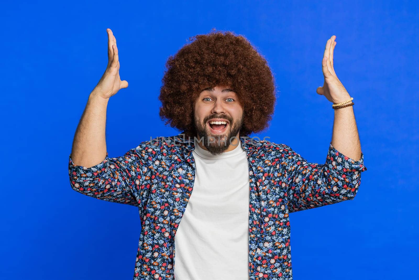 Shocked amazed surprised man with Afro hairstyle wig touching his head showing hands brain explosion wow gesture, professional burnout, celebrating success victory win. Guy isolated on blue background
