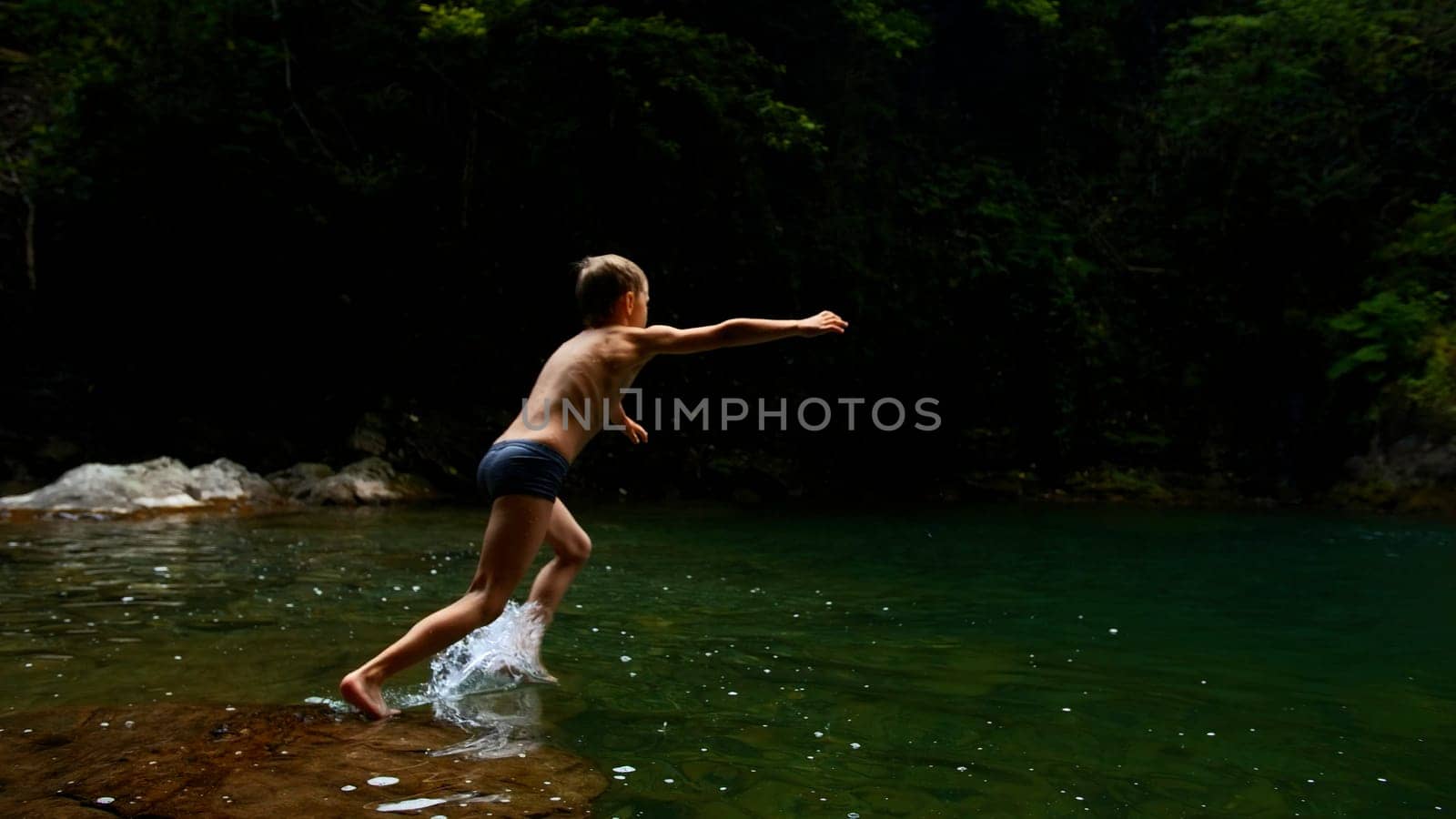 Boy child jumping in cold mountain river on a summer day. Creative. Hiking in summer jungles