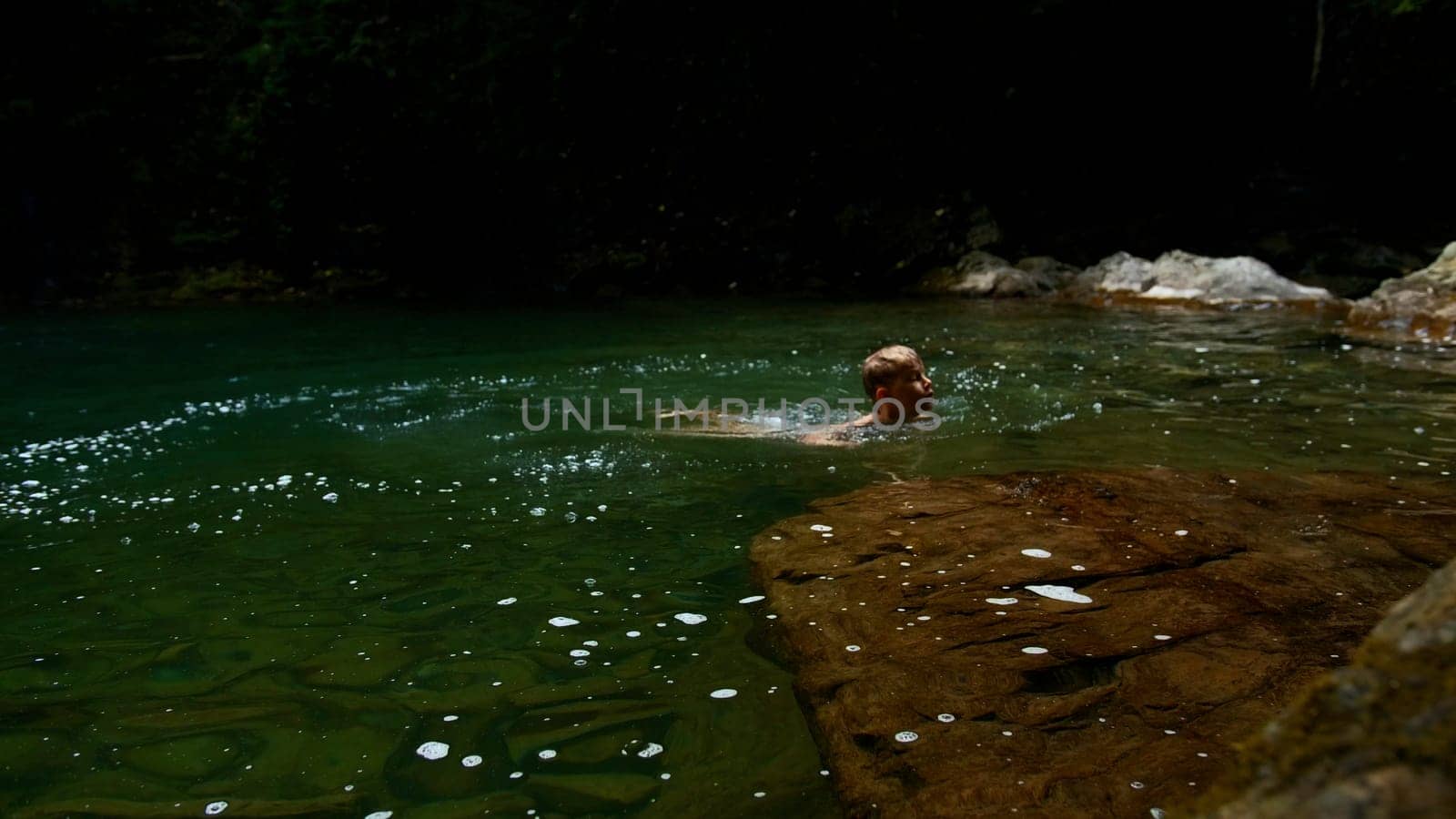 Slow motion of a boy jumping into a waterfall and natural pond. Creative. Young boy child having fun in jungles