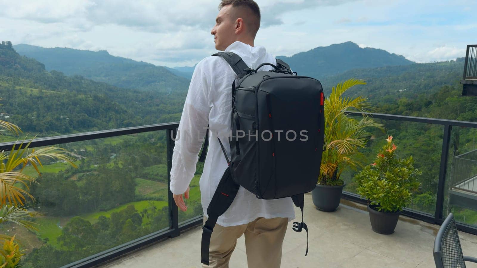 Man with view of tropical mountain valley. Action. Man on observation deck in tropical mountains. Man with backpack on sightseeing attraction overlooking green mountains.