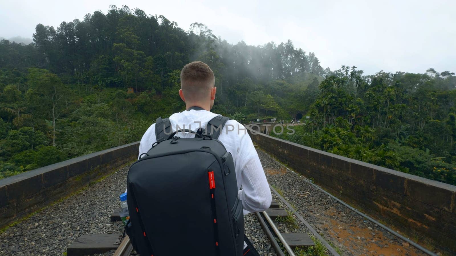 Man on hiking trip on tropical bridge. Action. Man on hiking trail with stone bridge and railway. Man walks on stone bridge in tropical mountains.