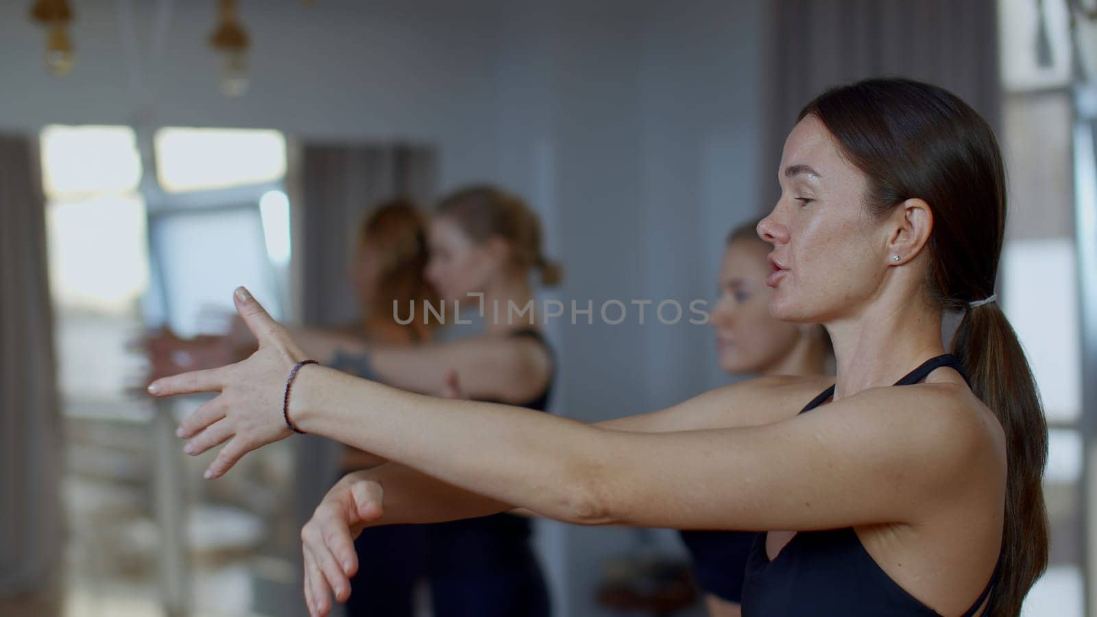 Woman coach performing training workout for female group. Media. Mentor explaining the technique of breathing with hands swings. by Mediawhalestock