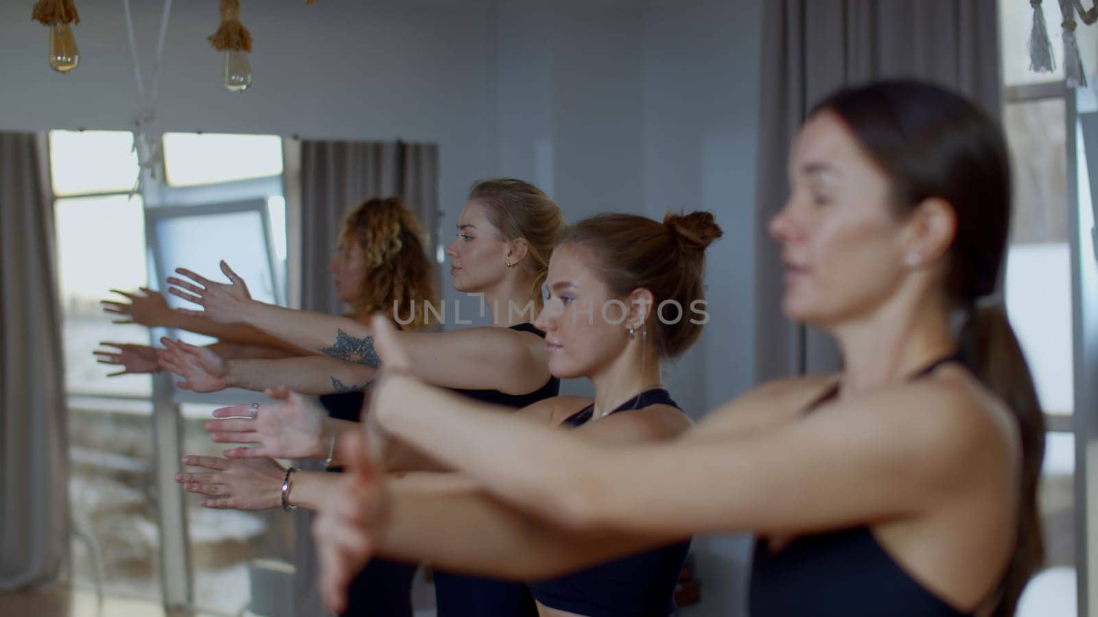 Relaxed sports team standing during group training in spacious studio. Media. Women breath deeply and swinging their hands, concept of yoga and relaxation