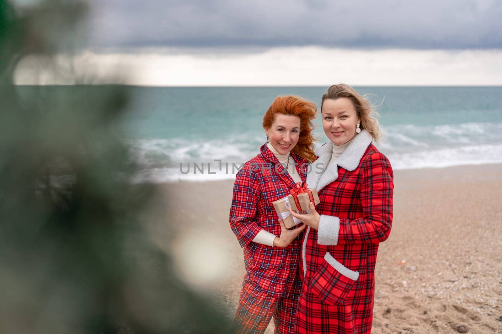 Sea two Lady in plaid shirt with a christmas tree in her hands enjoys beach. Coastal area. Christmas, New Year holidays concep by Matiunina