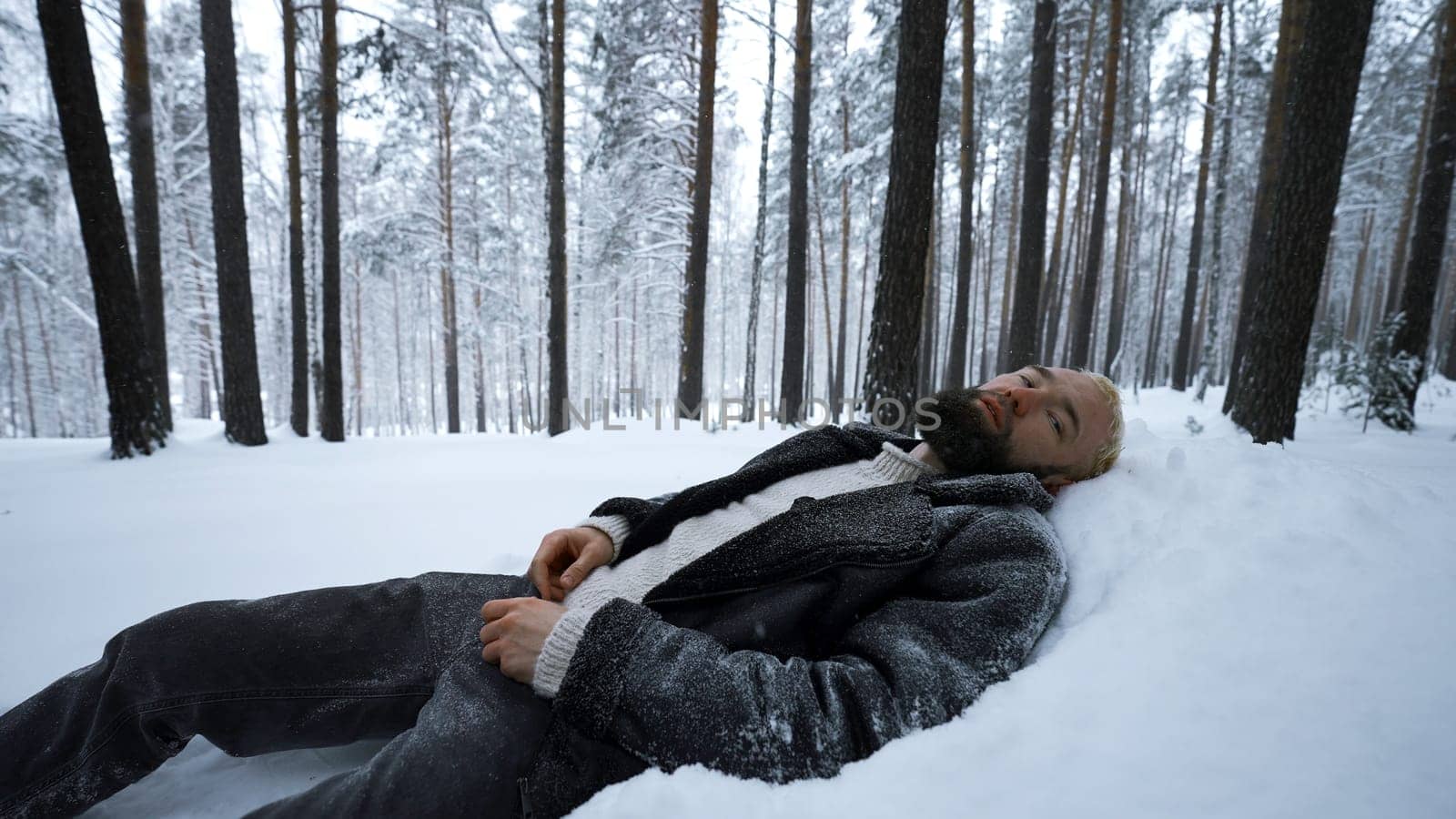 Man lies in snow in winter forest. Media. Tired man lies in snowdrift in winter forest. Depressive Stylish man lies in snow in winter forest.