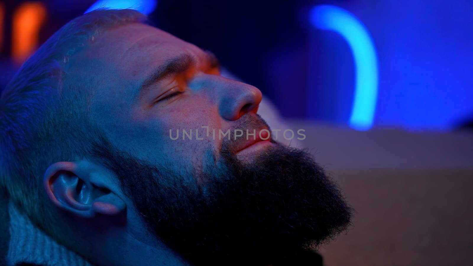 Portrait of a sleepy man with neon lighting. Media. Young bearded man feeling tired and trying to sleep