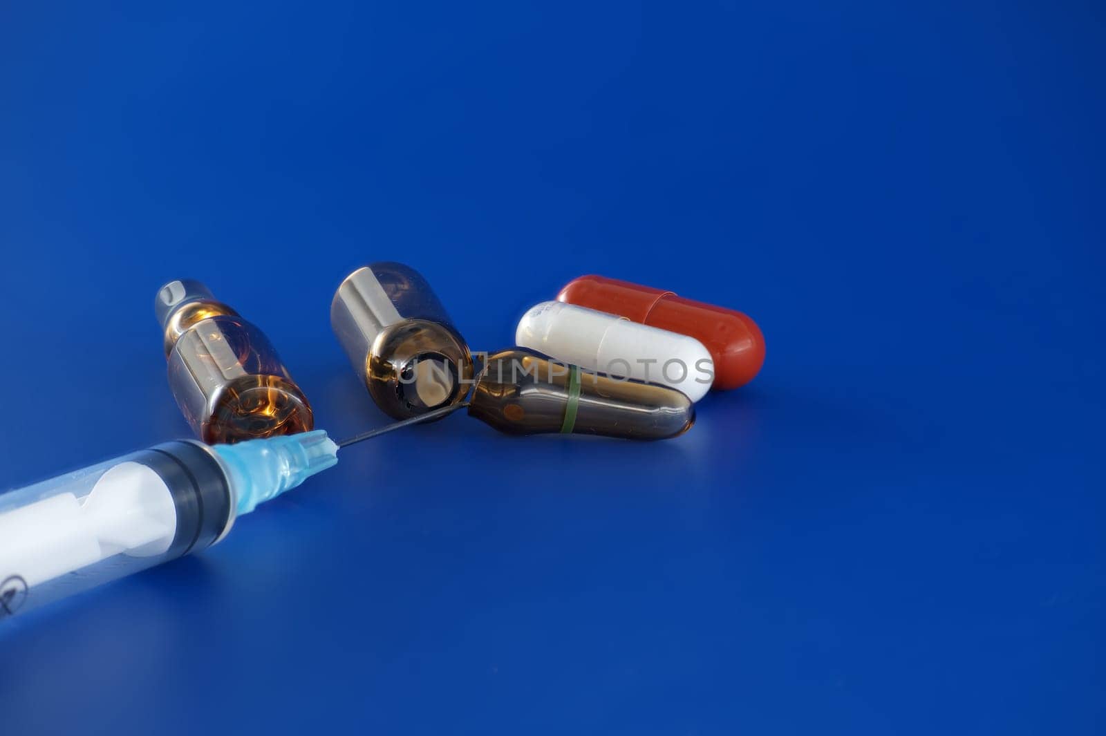 Syringe, ampoule and pills against a blue background, suggests oral medication as an alternative to the injectables