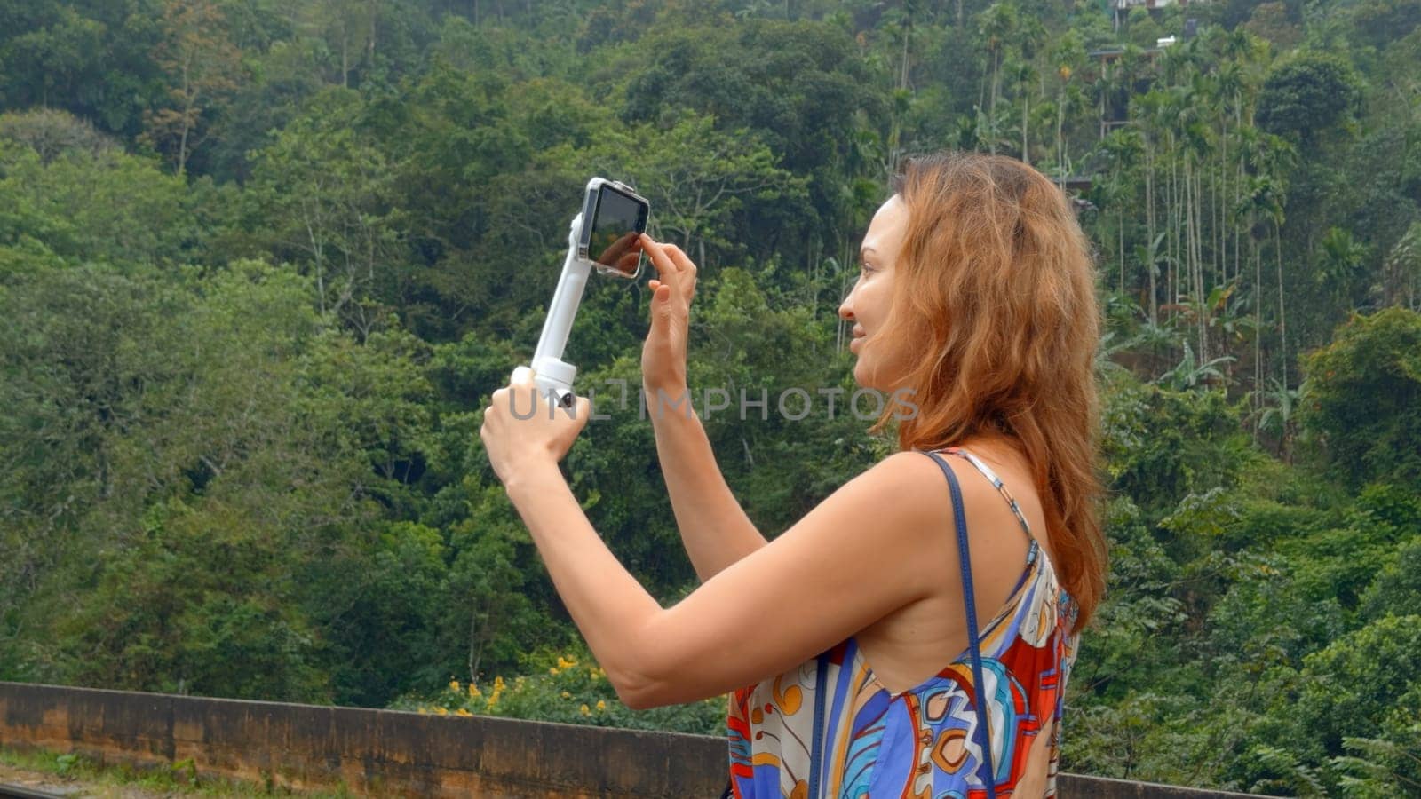 Beautiful woman takes pictures on phone with tripod. Action. Woman professionally shoots landscapes on phone while traveling for blog. Shooting for travel blog.