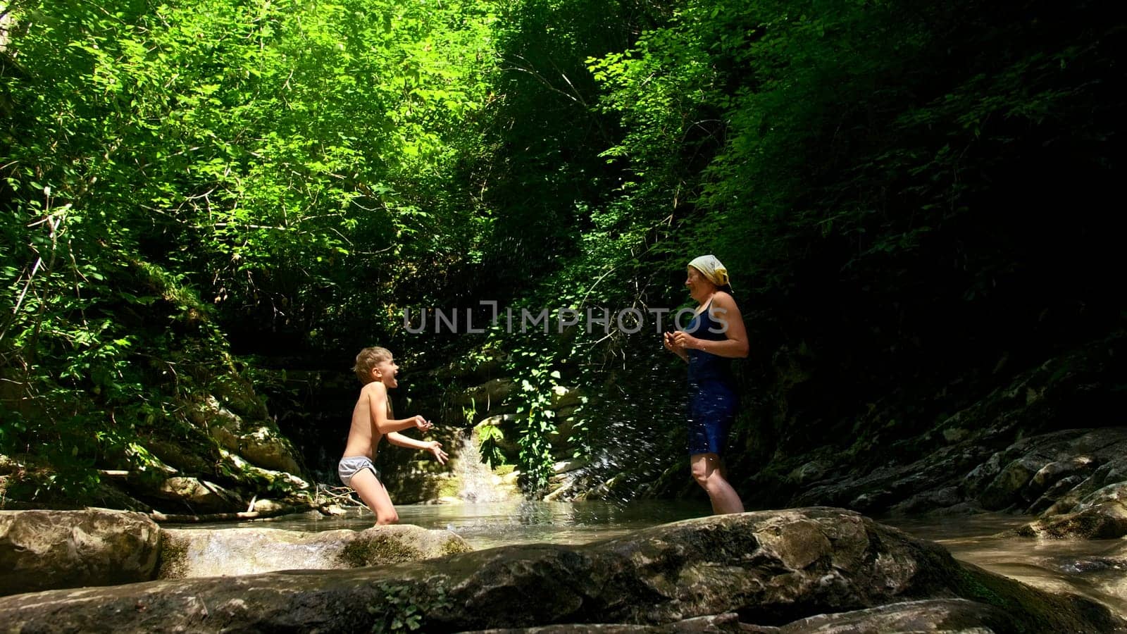 Mother with boy making water splashes in river and jungles on the background. Creative. Exploring natural beautiful places. by Mediawhalestock