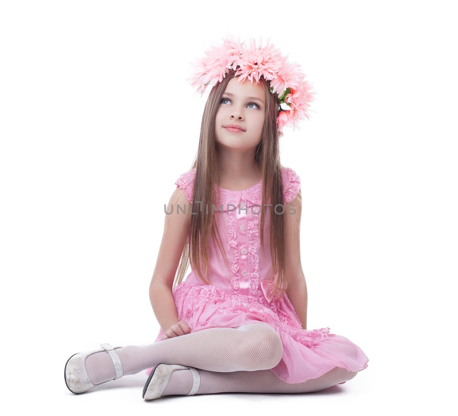 Little girl in pink dress and wreath sitting on floor. Isolated on white