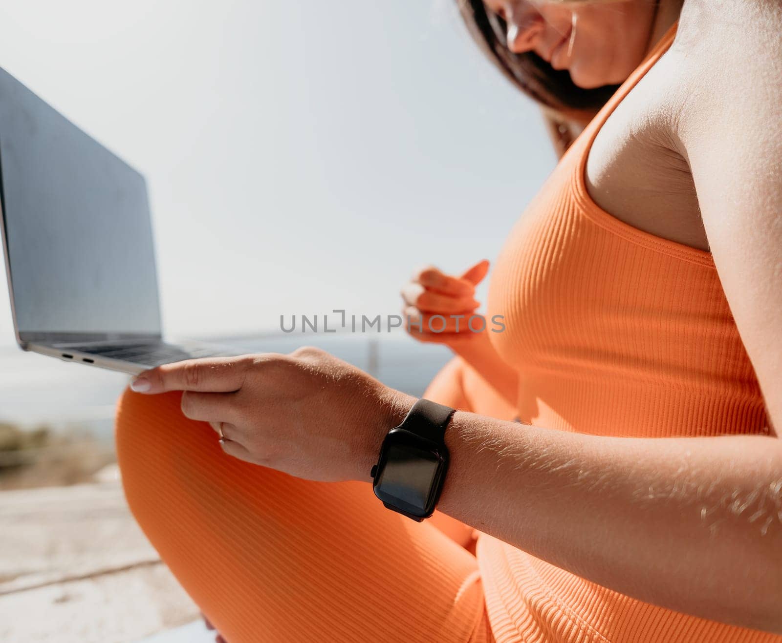 Digital nomad, Business woman working on laptop by the sea. Pretty lady typing on computer by the sea at sunset, makes a business transaction online from a distance. Freelance, remote work on vacation