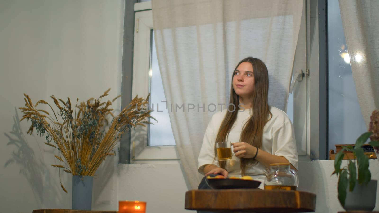 Young woman romantically drinks tea in cafe. Media. Young female student is relaxing in cafe with tea. Beautiful young woman is drinking tea alone in cozy cafe.