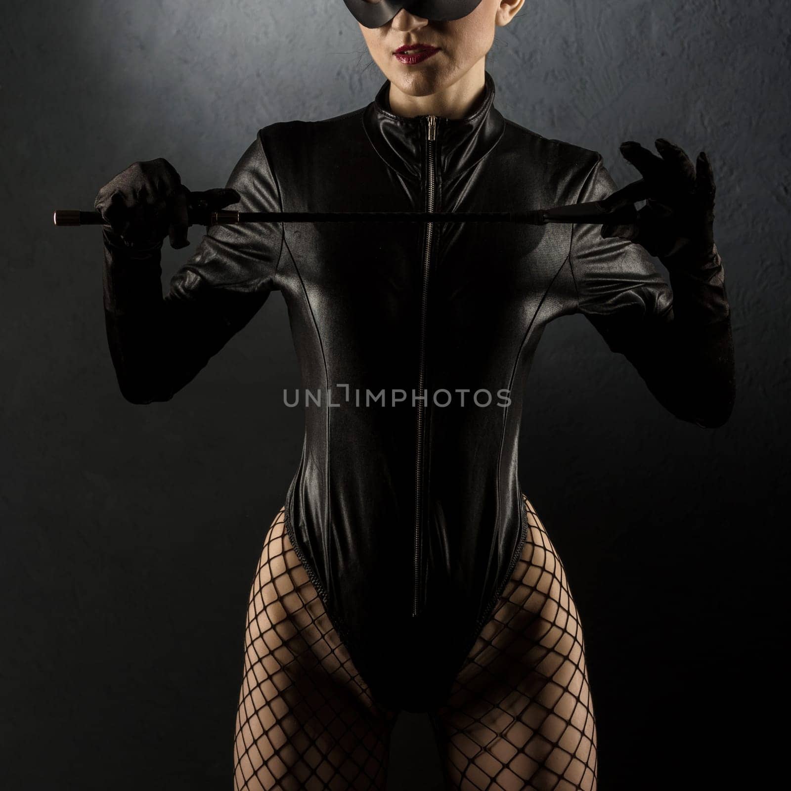 Adult sex games. Beautiful dominant brunette vamp mistress girl in latex body, gloves posing with riding crop. - image