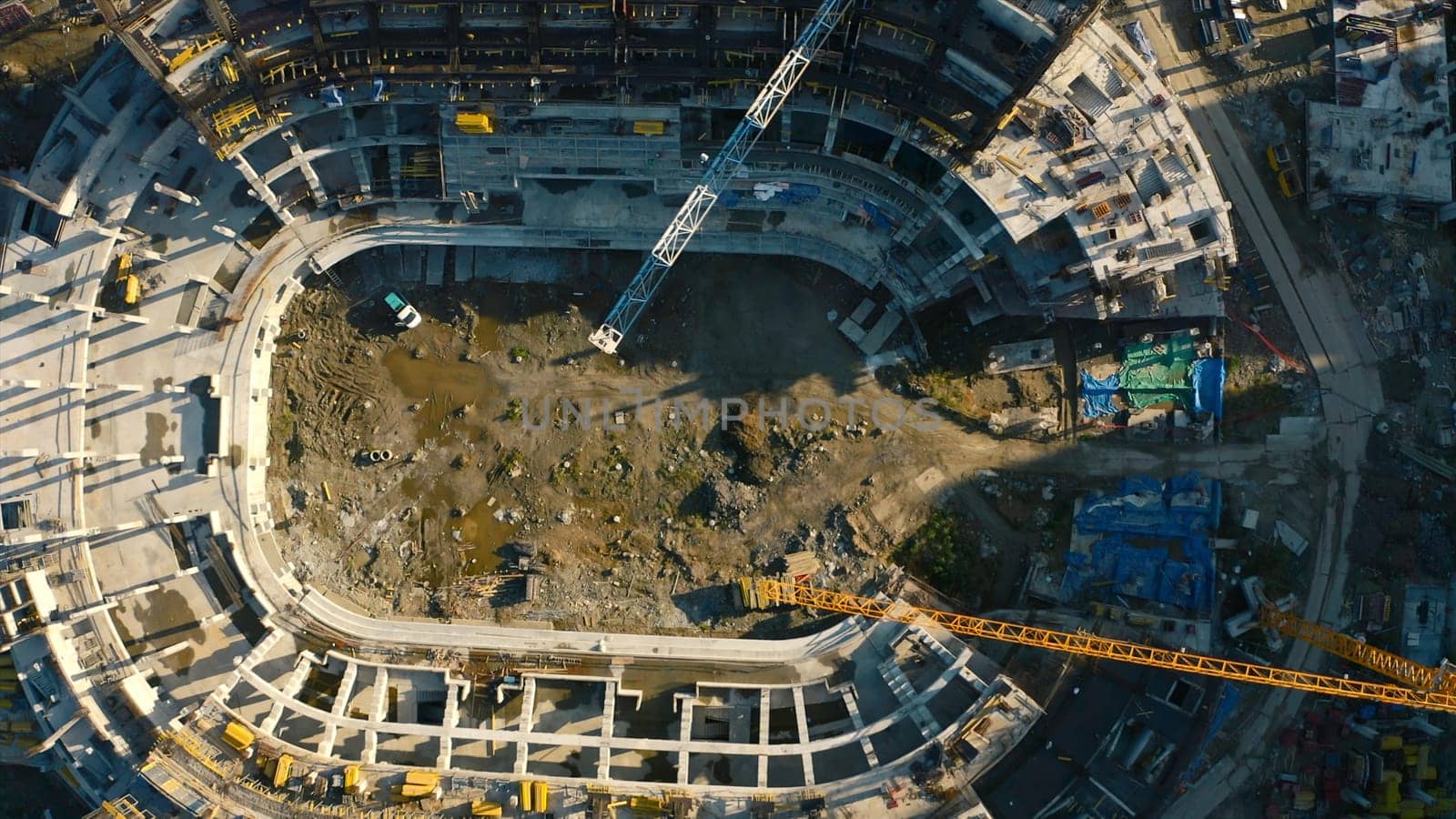 Vertical top view of construction of circular building. Stock footage. Construction site of building near parking lot in city center. Construction of stadium in center of residential city on sunny summer day.