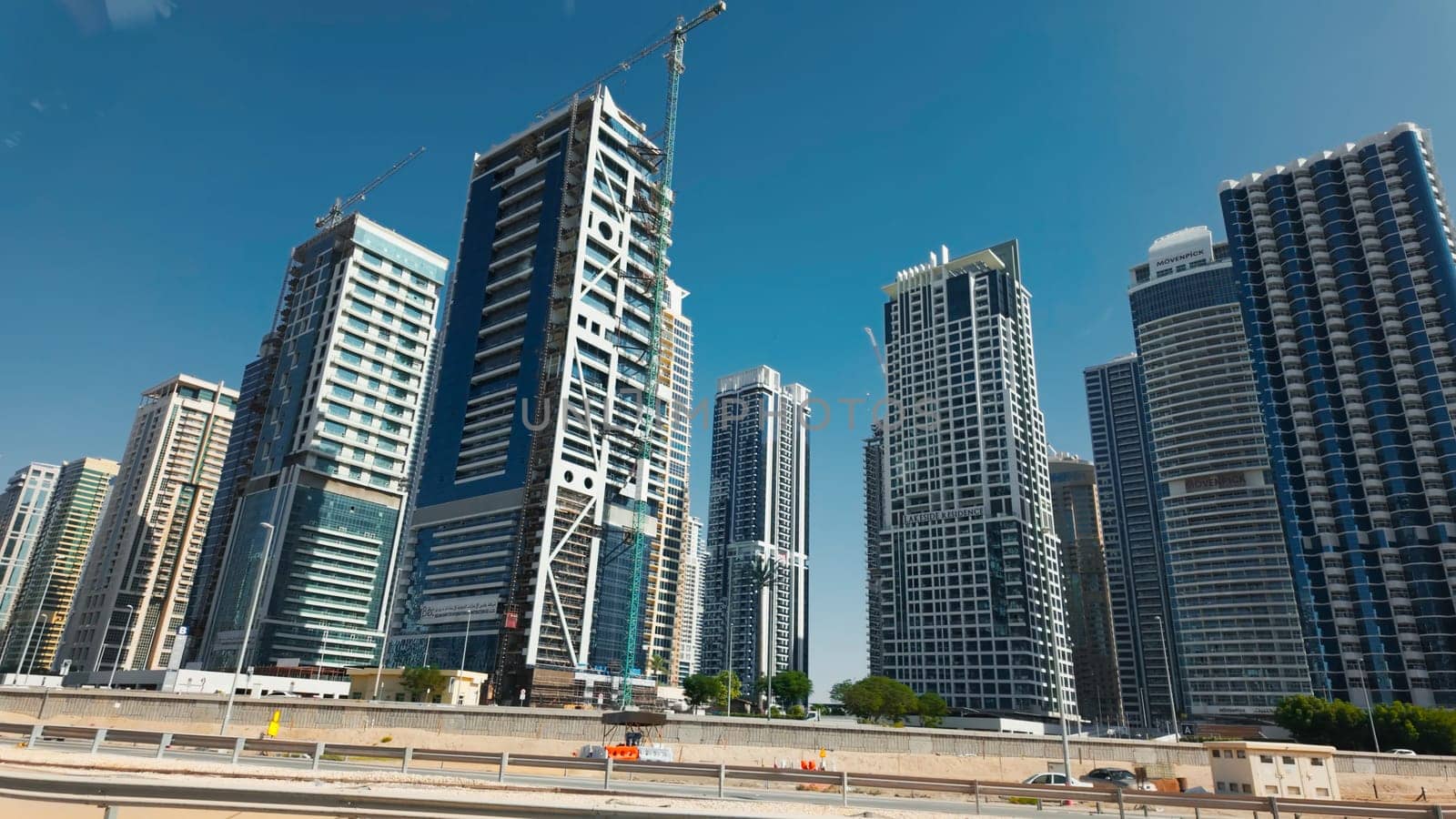 Dubai city with street and bridge with driving cars. Action. Clear blue sky and skyscrapers of the city center