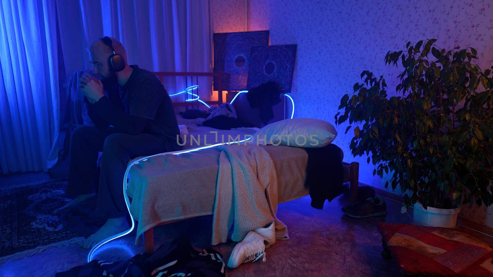 Depressed man sitting on his bed with headphones. Media. Young man feeling anxiety