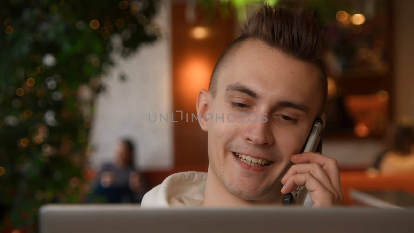 Young man is talking on phone on laptop. Stock footage. Handsome young man is talking on phone and working on laptop. Freelancer on remote with phone and laptop in cafe by Mediawhalestock