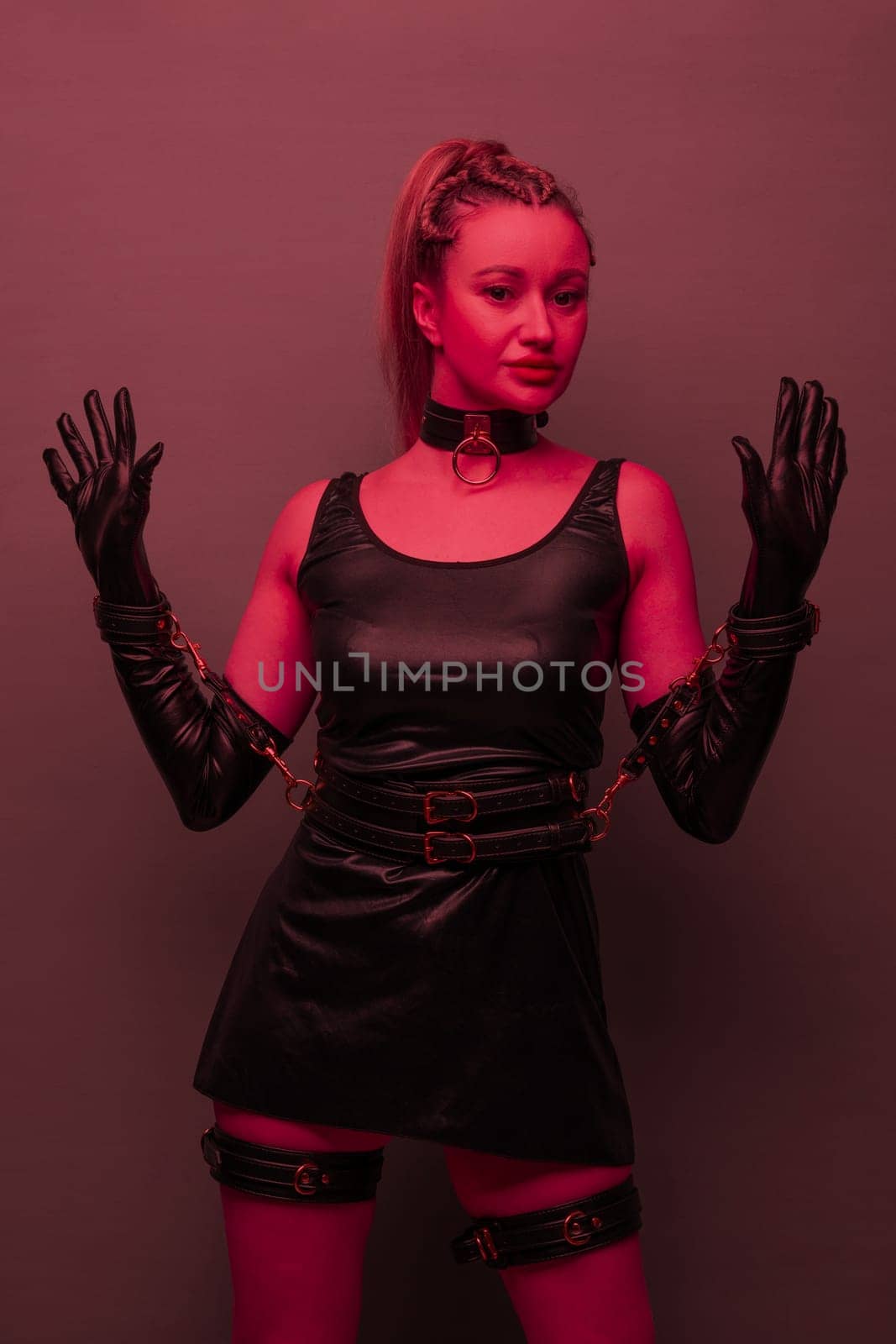 Beautiful young woman in a leather dress and bondage set posing on red light backgound