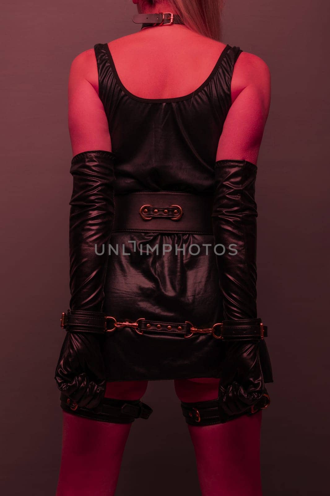 Beautiful young woman in a leather dress and bondage set posing back on red light backgound