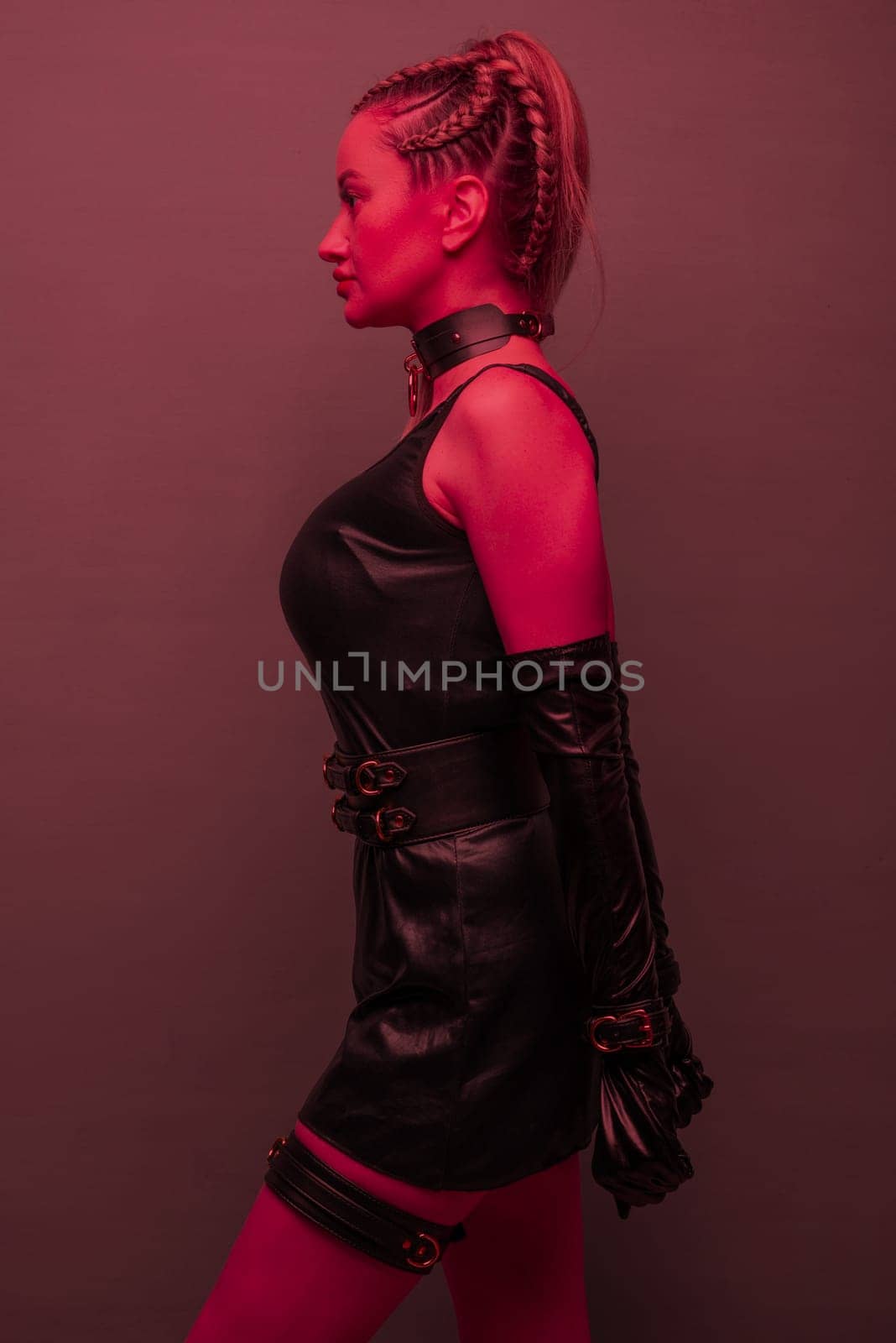 Beautiful young woman in a leather dress and bondage set posing on red light backgound