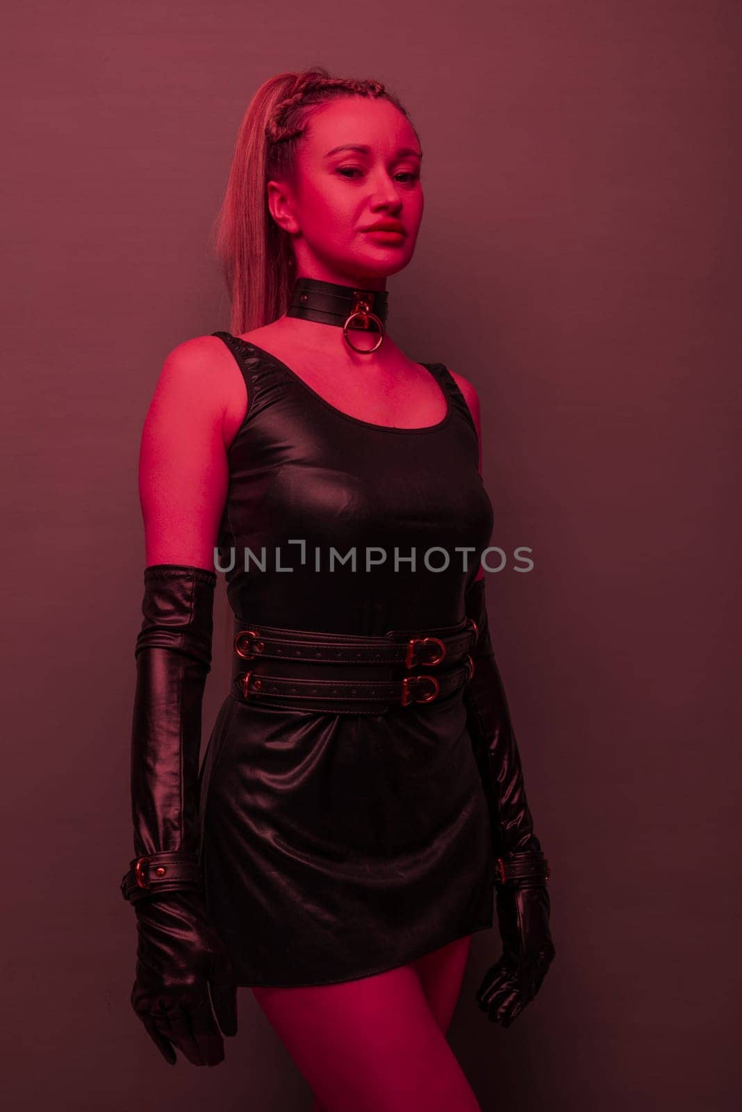 Beautiful young woman in a leather dress and bondage set posing on red light backgound by zartarn