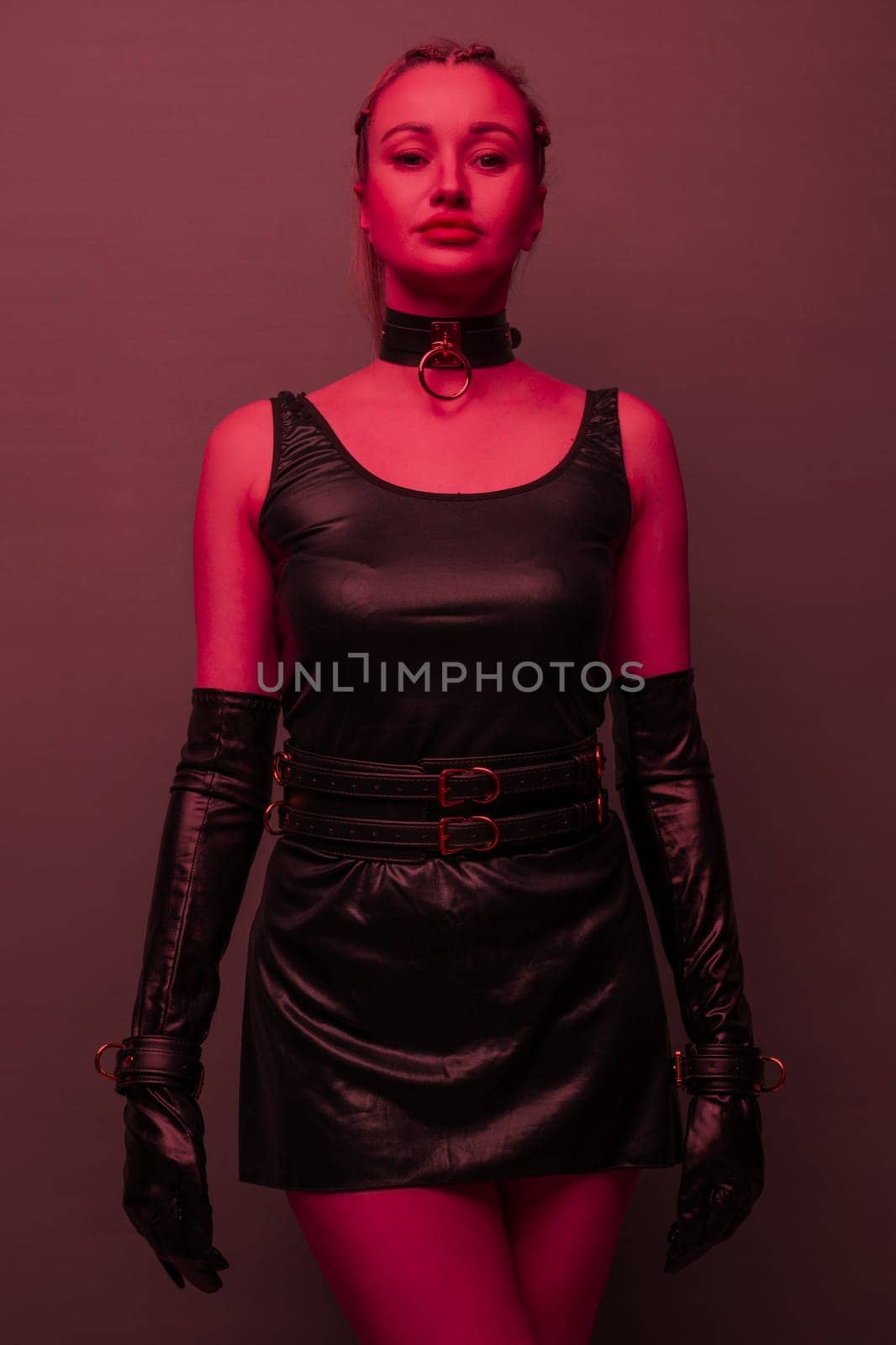 Beautiful young woman in a leather dress and bondage set posing on red light backgound by zartarn