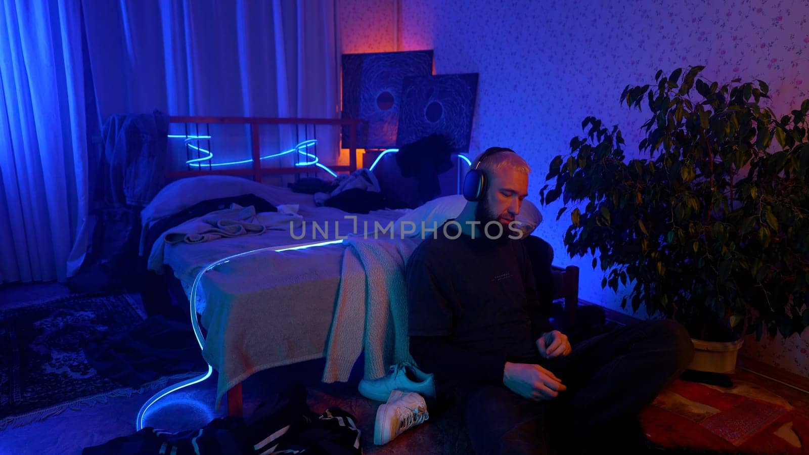 Young man in hipster room with neon lighting listening to music. Media. Man enjoying music with headphones on his head
