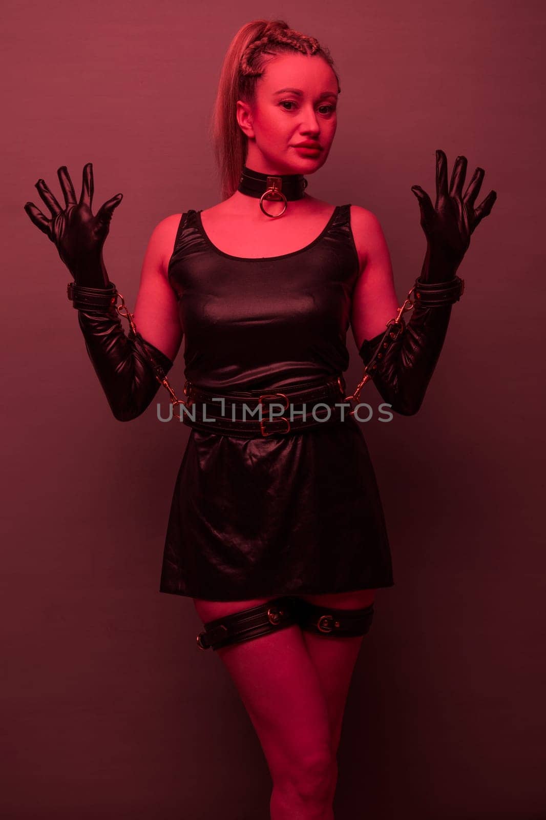 Beautiful young woman in a leather dress and bondage set posing on red light backgound