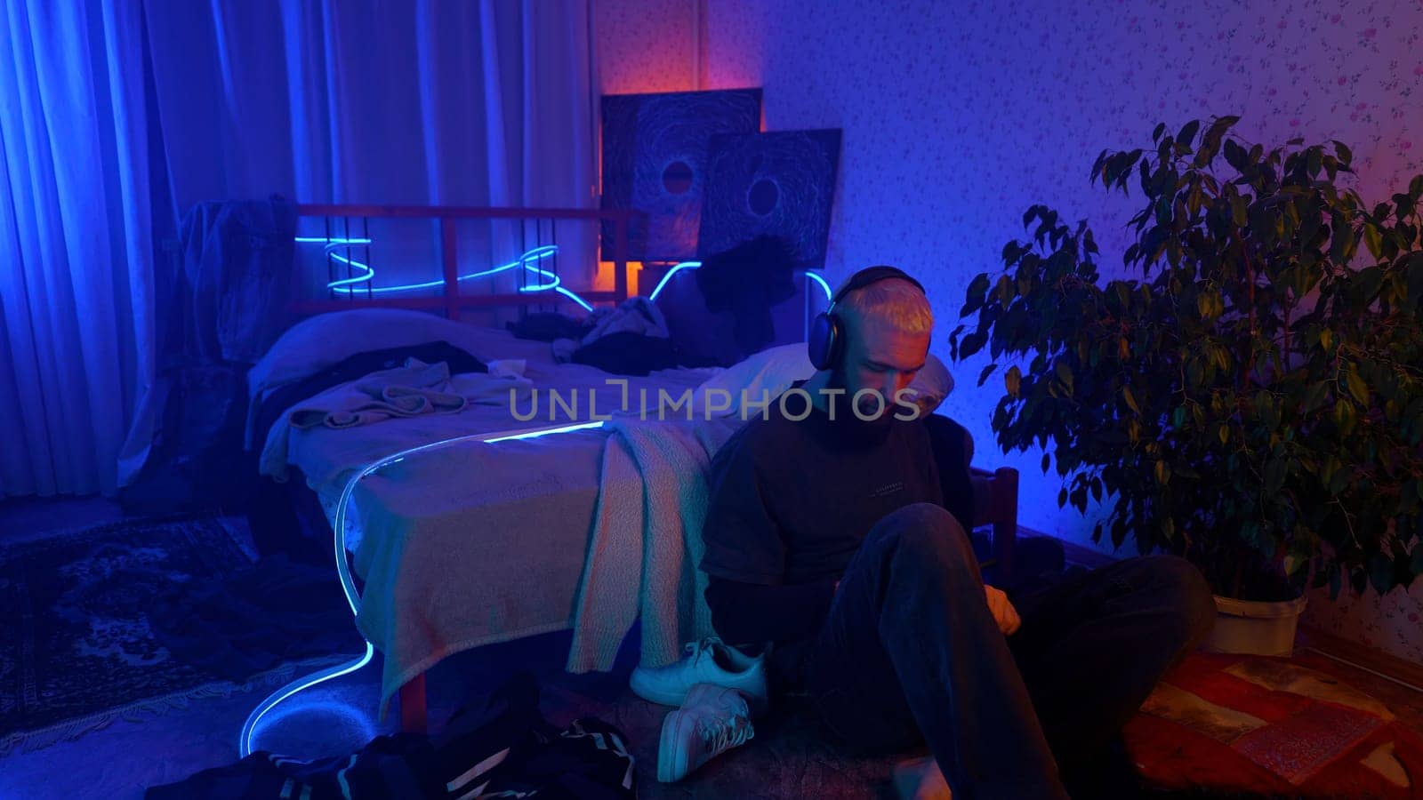 Bearded caucasian young relaxed man is sitting on floor in cozy evening room and listening to music. Media. Relax and home leisure