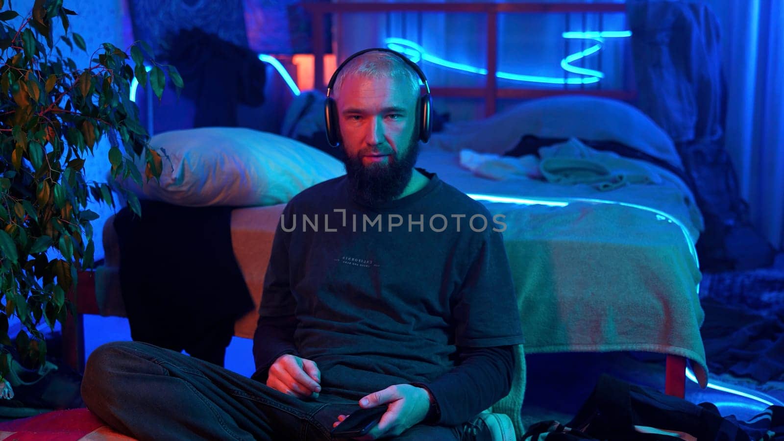 A guy in a neon room listening to music alone and relaxing. Media. Room of a teenager and mess