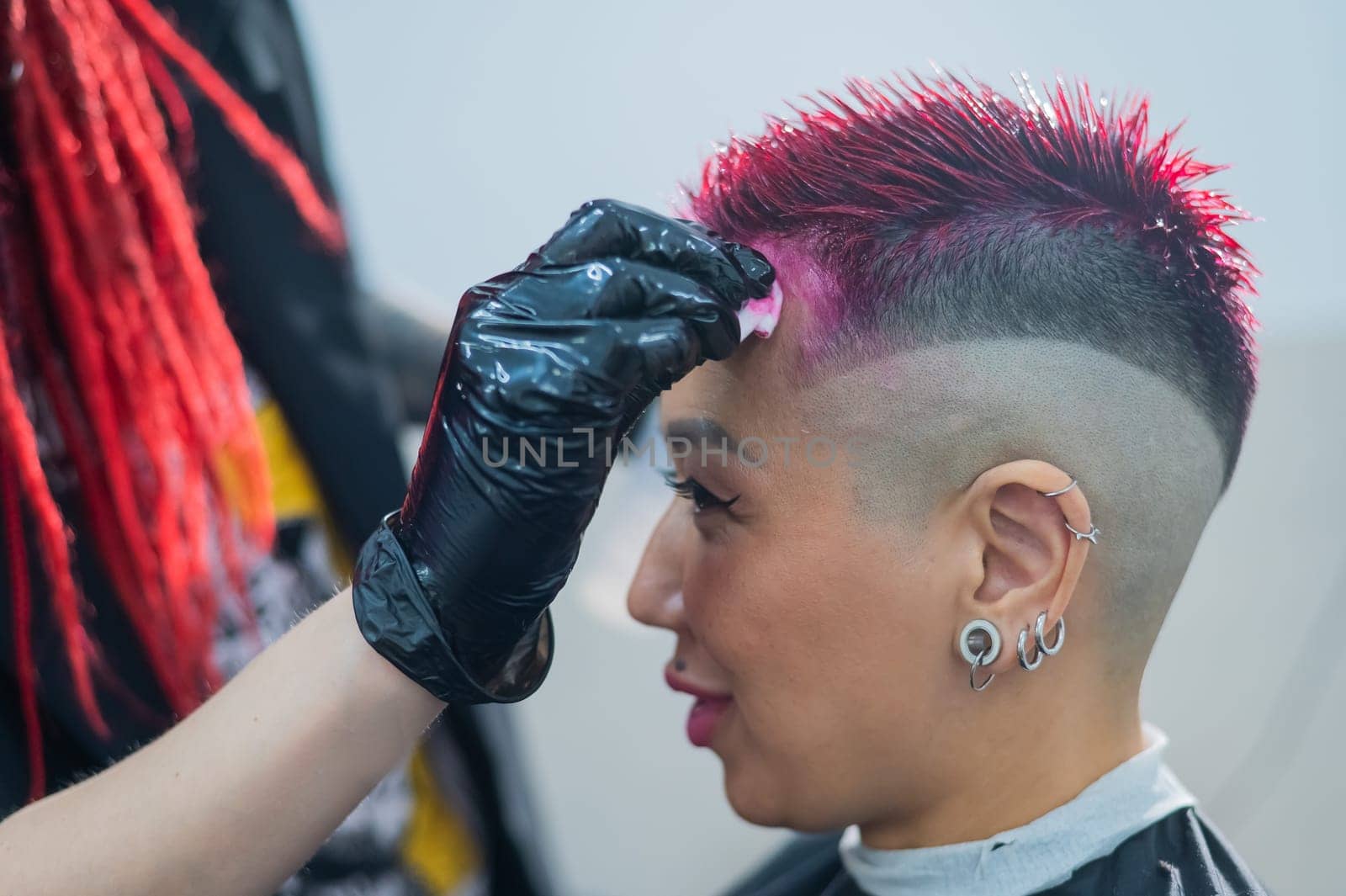 The hairdresser removes excess dye from the skin of a female with a cotton pad.Asian woman with a short haircut in a hairdressing salon. by mrwed54