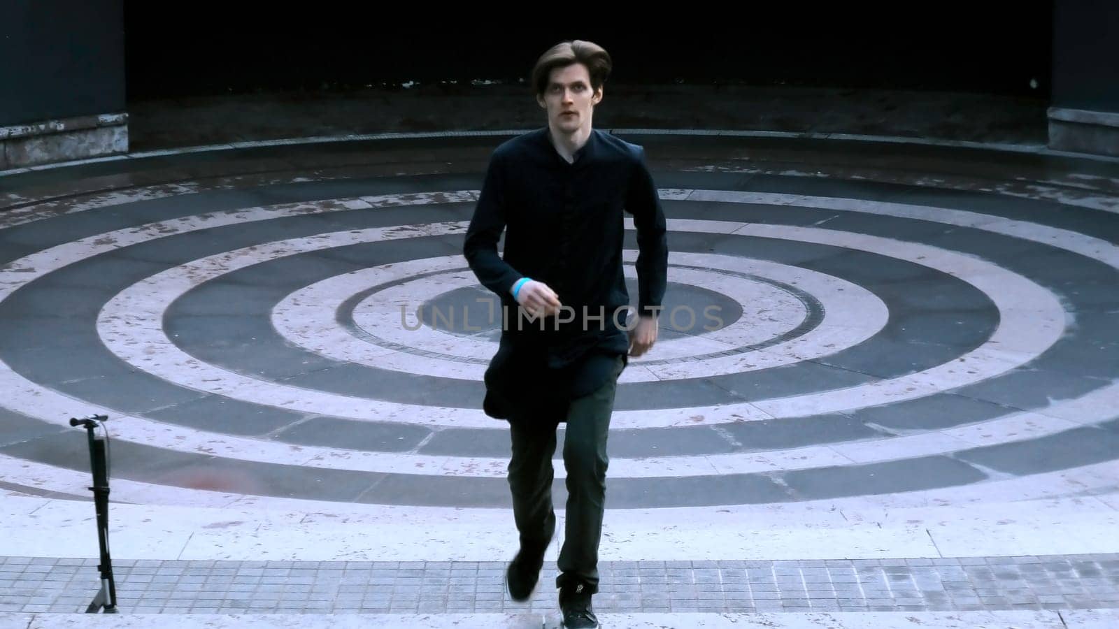 Young man dressed in black running up the stairs of stone amphitheater. Stock clip. Asphalt painted in white and black rings. by Mediawhalestock