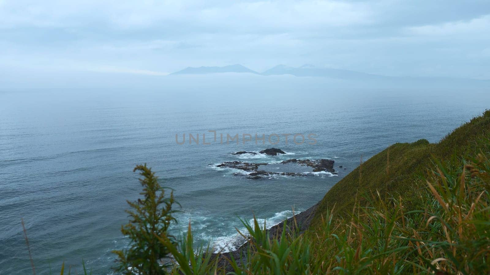 Beautiful landscape from top of green mountain to sea horizon on cloudy day. Clip. Beautiful green grass on mountain ridge of sea coast. Line of mountain coast with green grass and sea horizon on cloudy day.