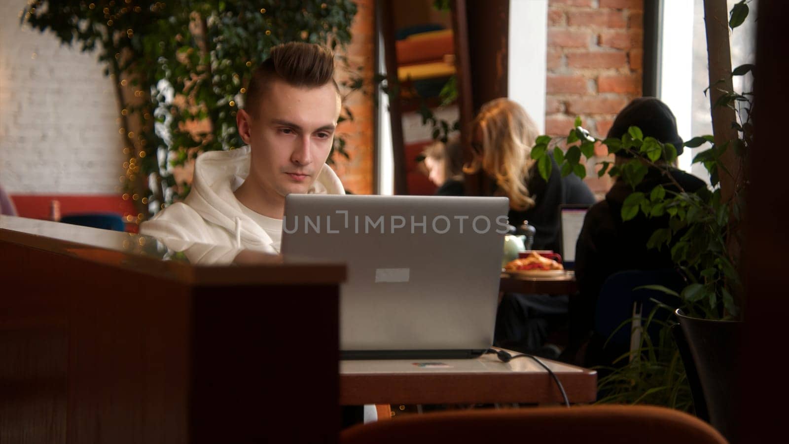 Tired young man is working on laptop in cafe. Stock footage. Handsome young man is writing diploma on laptop in cafe. Young freelancer or student is working on laptop in cafe.
