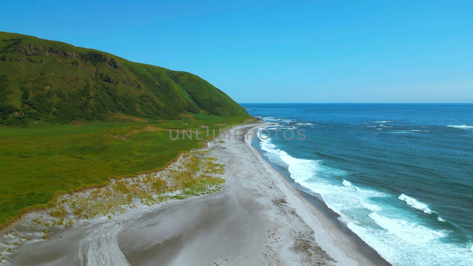 Breathtaking aerial view of the summer beach coastline. Clip. Wild empty sea shore and green fields