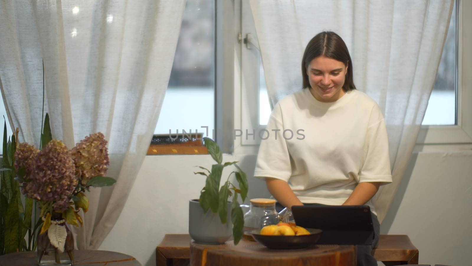 Young woman drinks tea and looks at tablet in cafe. Media. Student watches video on break and drinks tea in cozy cafe. Young woman is relaxing watching tablet and having tea in cafe.