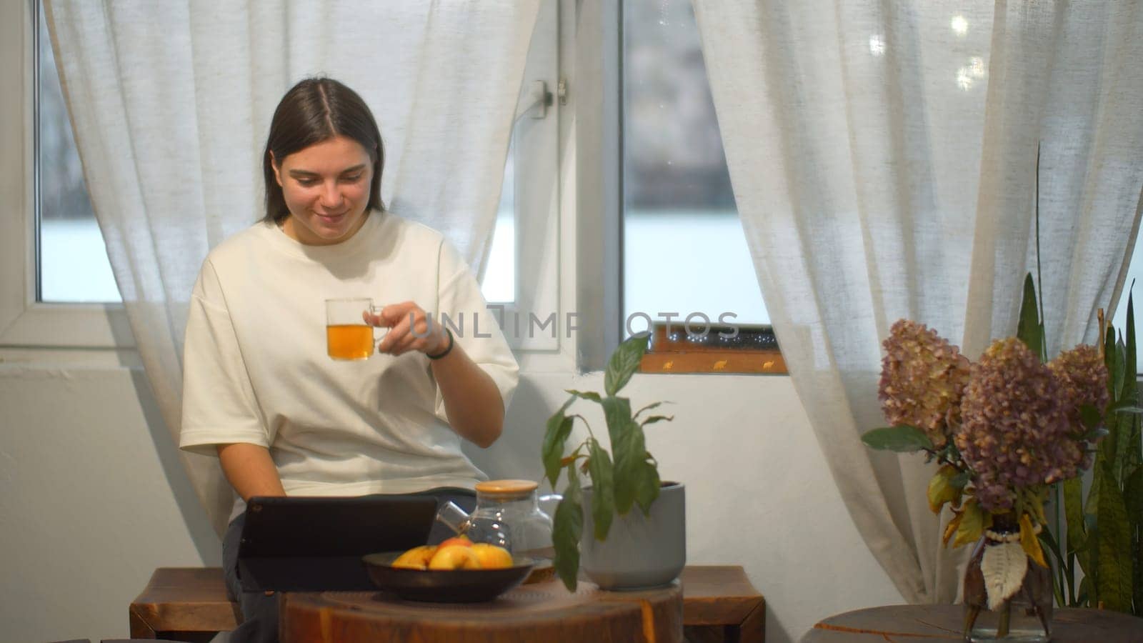 Young woman drinks tea and looks at tablet in cafe. Media. Student watches video on break and drinks tea in cozy cafe. Young woman is relaxing watching tablet and having tea in cafe by Mediawhalestock