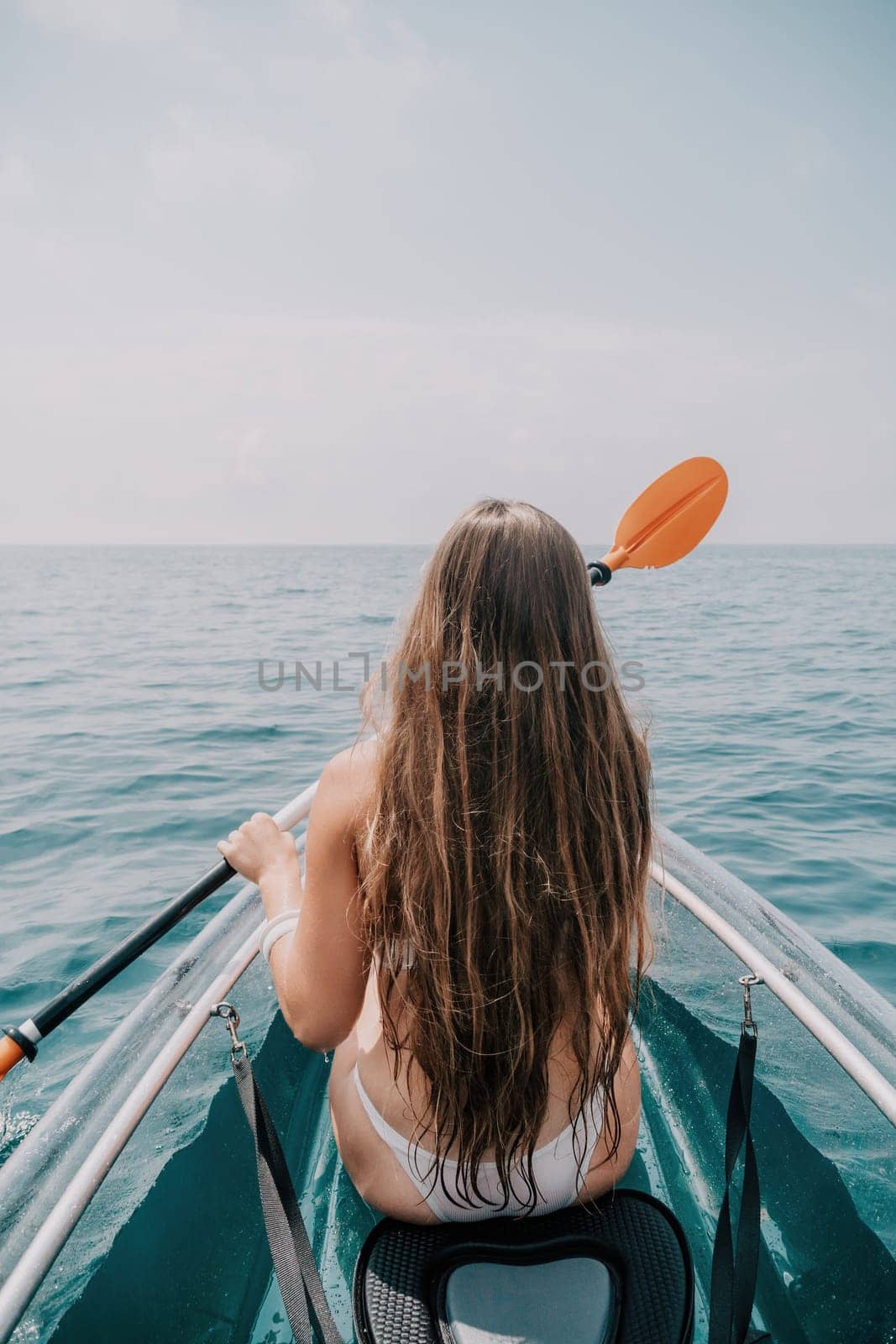 Woman in kayak back view. Happy young woman with long hair floating in transparent kayak on the crystal clear sea. Summer holiday vacation and cheerful female people having fun on the boat.