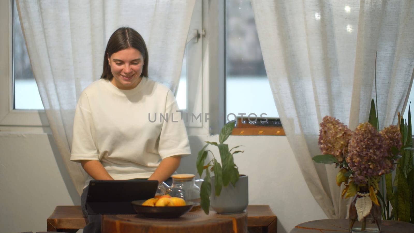 Young woman drinks tea and looks at tablet in cafe. Media. Student watches video on break and drinks tea in cozy cafe. Young woman is relaxing watching tablet and having tea in cafe.