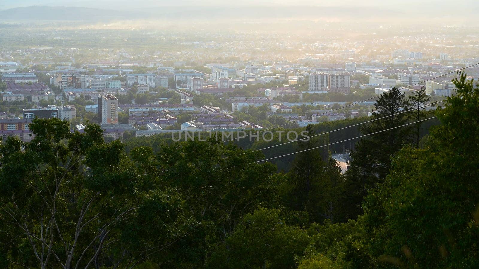 Beautiful view of cable car with view of town in summer. Clip. Green forest on slope with moving cable ways on edge of town. Beautiful city in valley with cable car on sunny summer day.