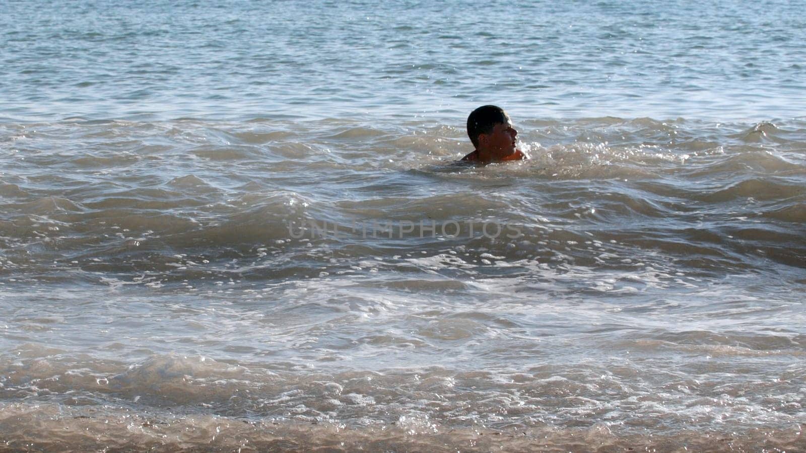 Happy child enjoys swimming in the sea on a hot summer day. Creative. Strong waves and boy in water