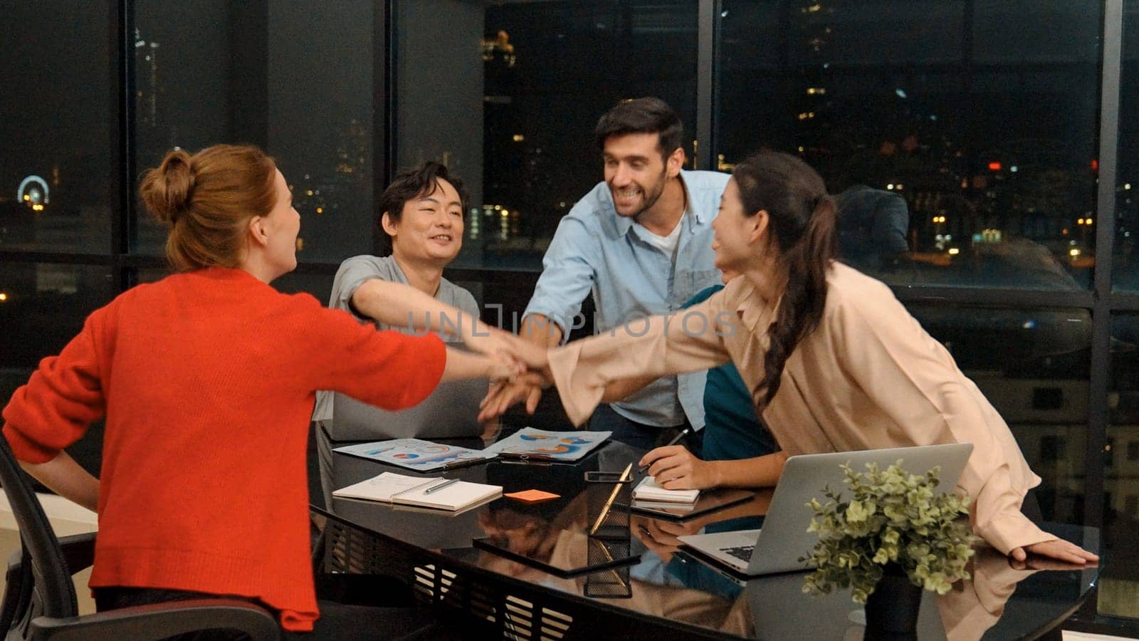 Businesspeople putting hands together and clapping hands to celebrate successful project at modern office with night city view. Group of manager with stacks of hands. Teamwork, trust. Tracery