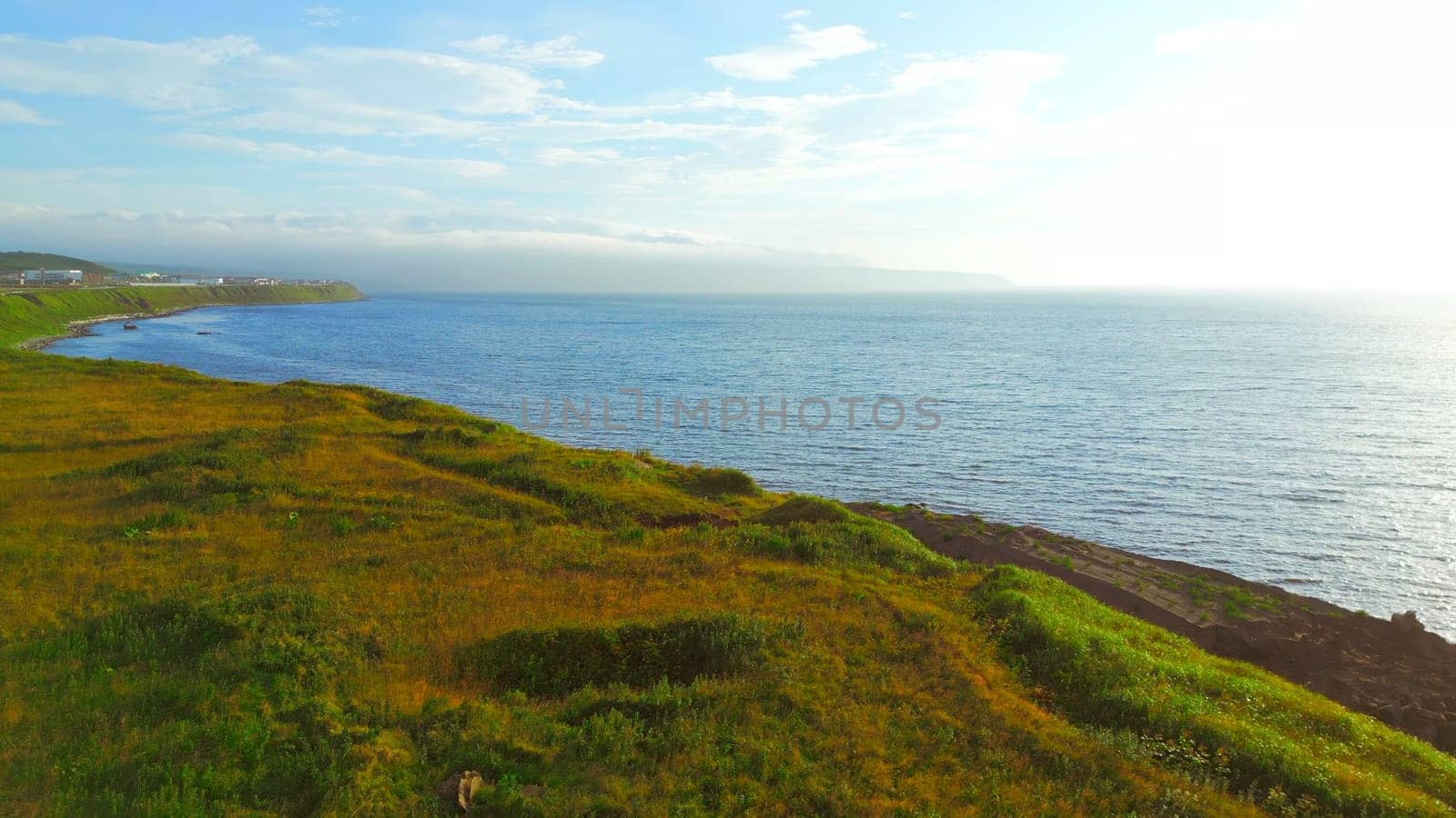 Beautiful coast with road and sea horizon on sunny day. Clip. Top view of seascape of coast on sunny summer day. Road to coast with view of sunny sea horizon.