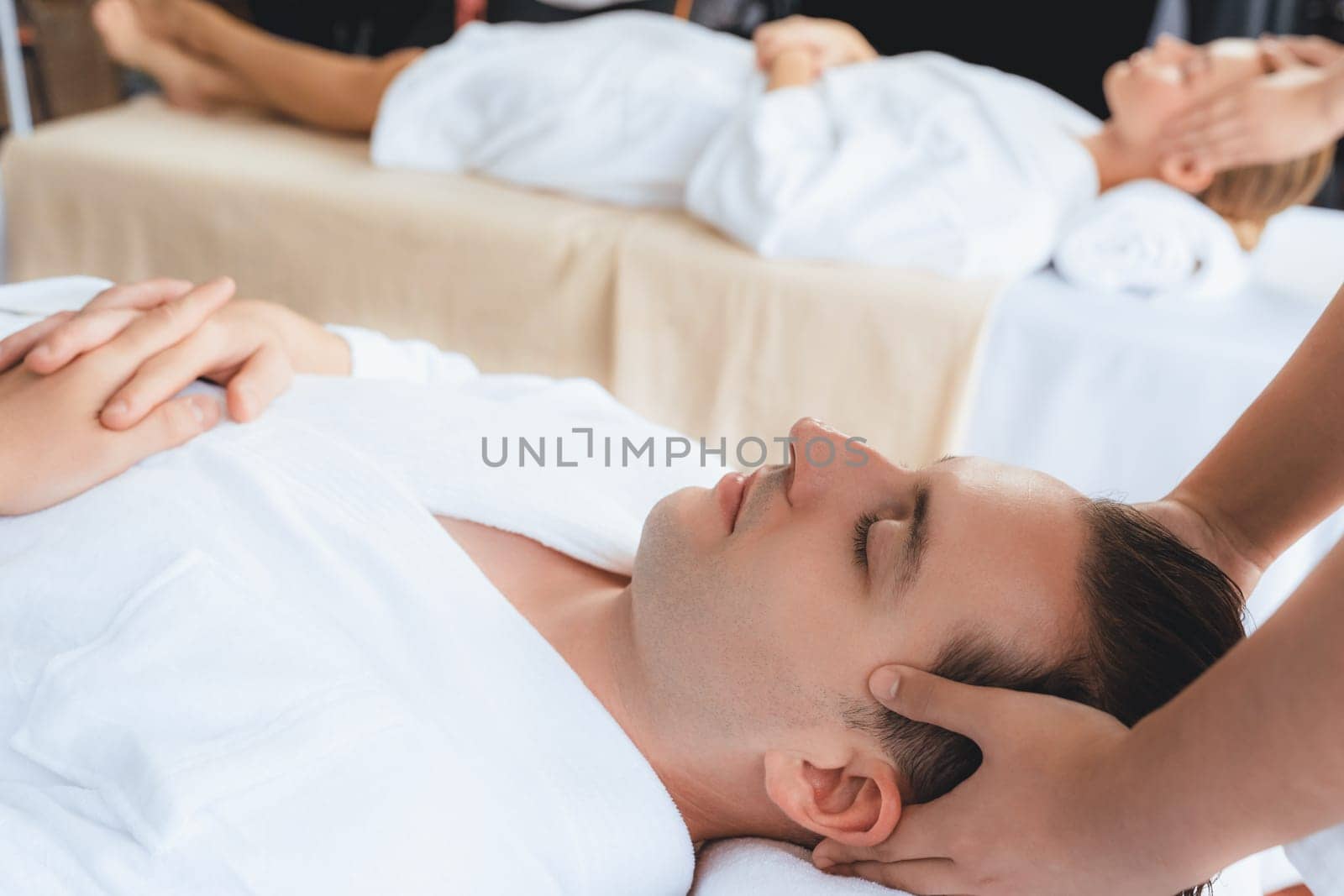 Caucasian couple enjoying relaxing anti-stress head massage and pampering facial beauty skin recreation leisure in dayspa modern light ambient at luxury resort or hotel spa salon. Quiescent