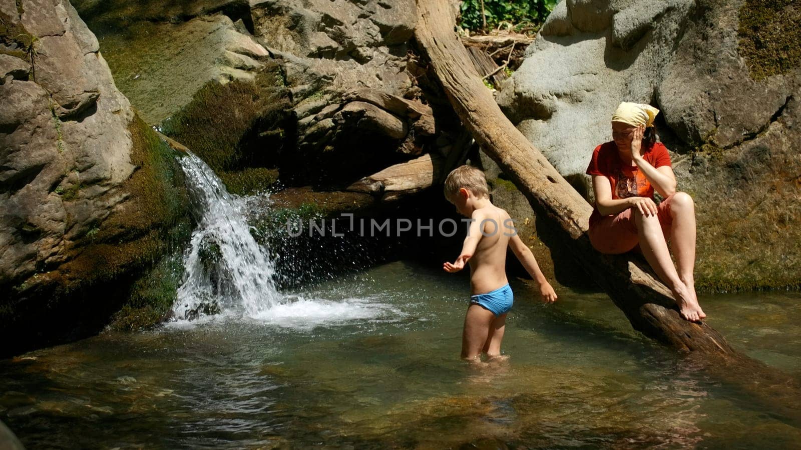 Mom with boy child in tropical waterfall. Creative. Family of hikers on a summer trip in jungles. by Mediawhalestock