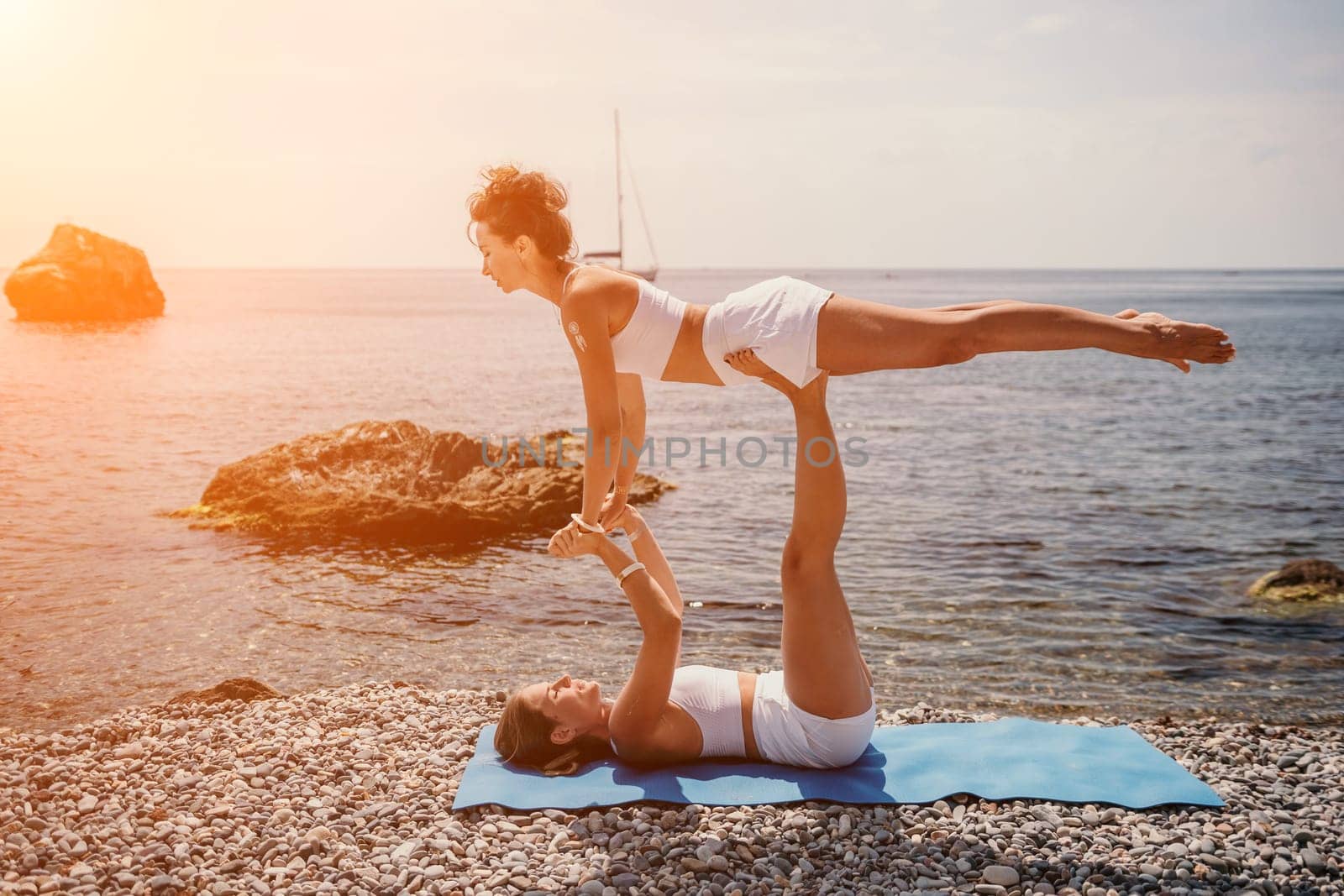 Woman sea yoga. Two happy women practicing yoga on the beach with ocean and rock mountains. Motivation and inspirational fit and exercising. Healthy lifestyle outdoors in nature, fitness concept. by panophotograph