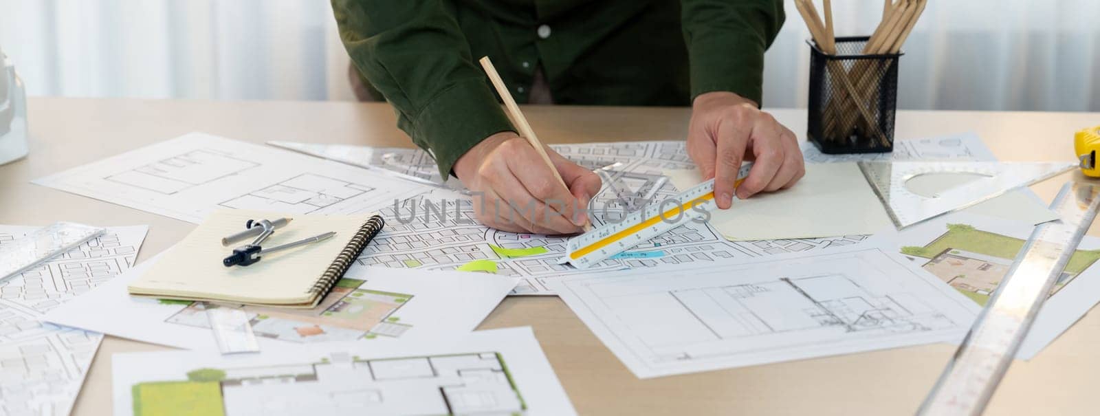 A portrait of architect using divider to measure blueprint. Architect designing house construction on a table at studio, with architectural equipment scattered around. Focus on hand. Delineation