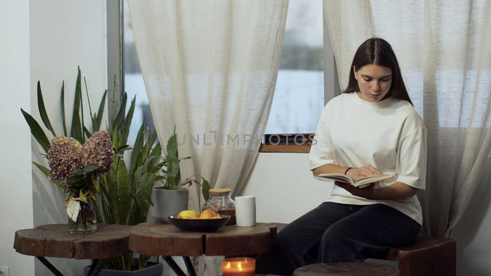 Young woman drinking tea in a kitchen at home. Media. Attractive lady enjoying cup of green tea and reading a book